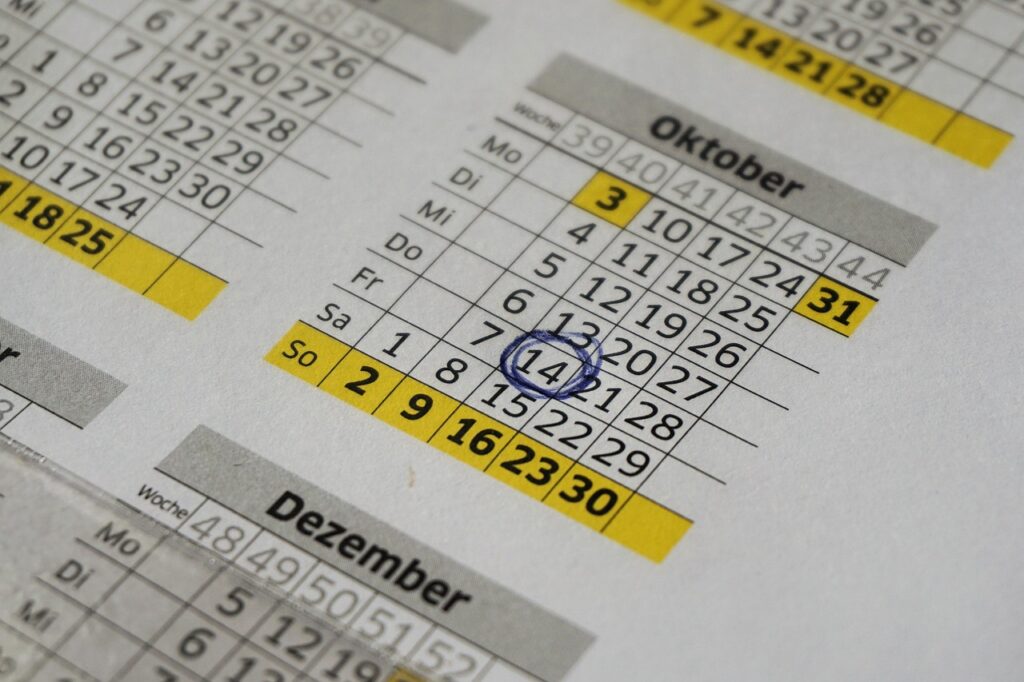 Kalender mit markiertem Datum neben Laptop und Notizzettel